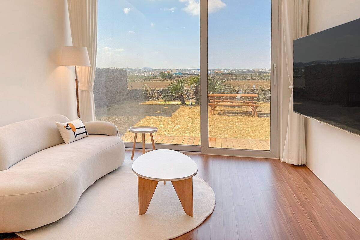 A modern living room with a sofa, a small round table, and a large window offering a view of a dry landscape.
