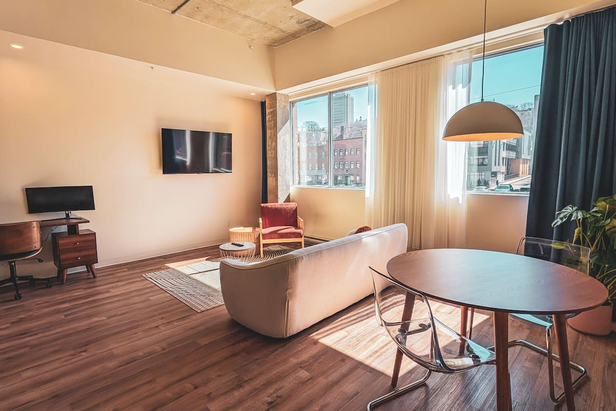 Uma sala de estar moderna com sofá, mesa de jantar, TV e uma grande janela com vista para a cidade.