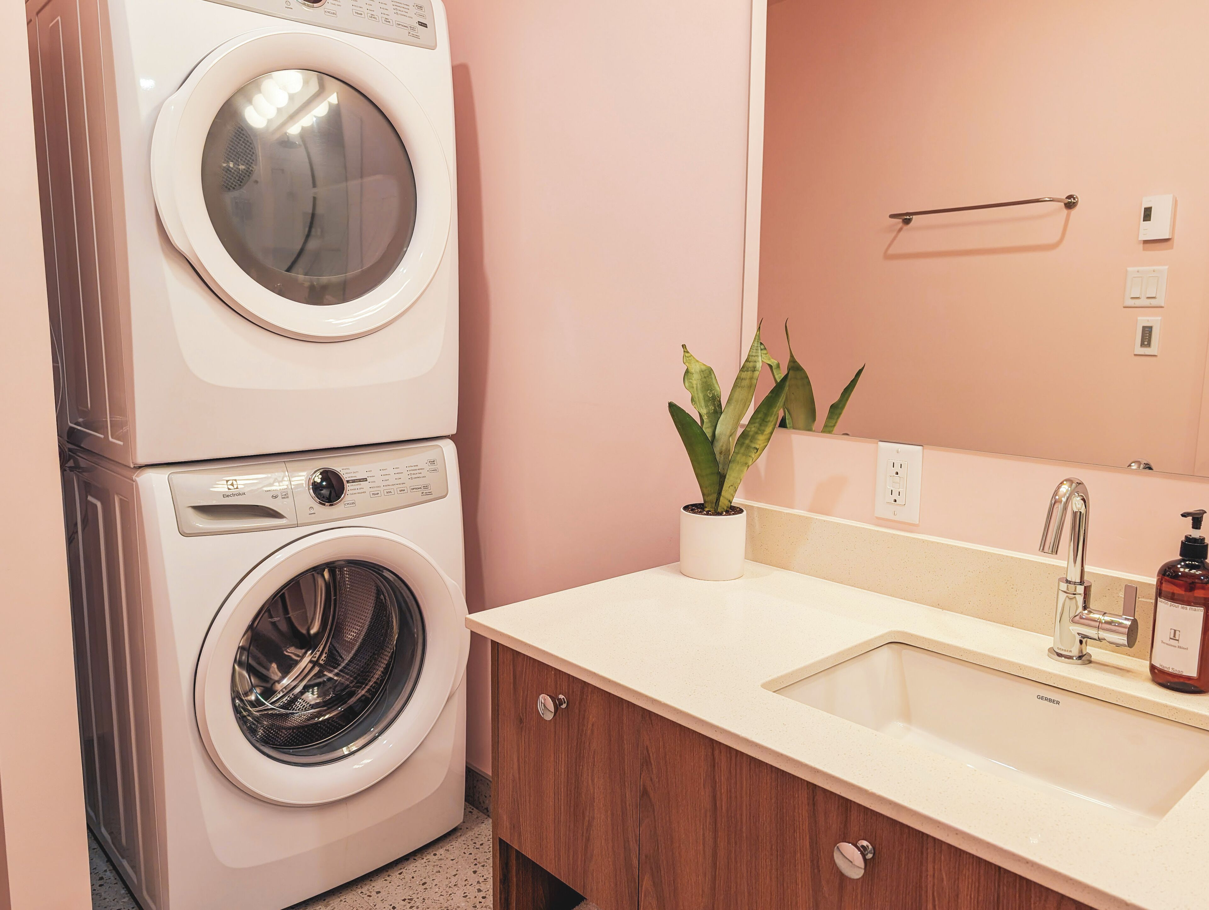 A laundry room with a stacked washer and dryer, a sink with a mirror, and a potted plant.