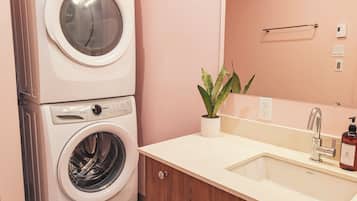A laundry room with a stacked washer and dryer, a sink with a mirror, and a potted plant.