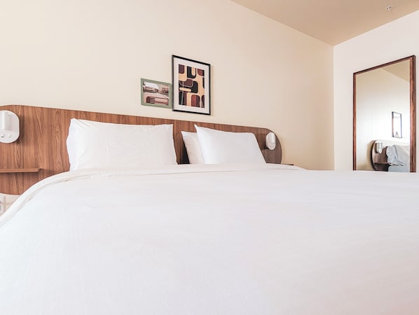 A hotel room with a wooden headboard, a large bed with white bedding, two framed pictures on the wall, and a mirror on the right side. - Terminus Hôtel (Québec)