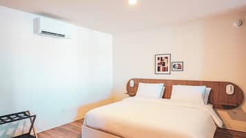 Een slaapkamer met een houten hoofdbord, een bed met wit beddengoed, een klein nachtkastje en een wandairconditioner.