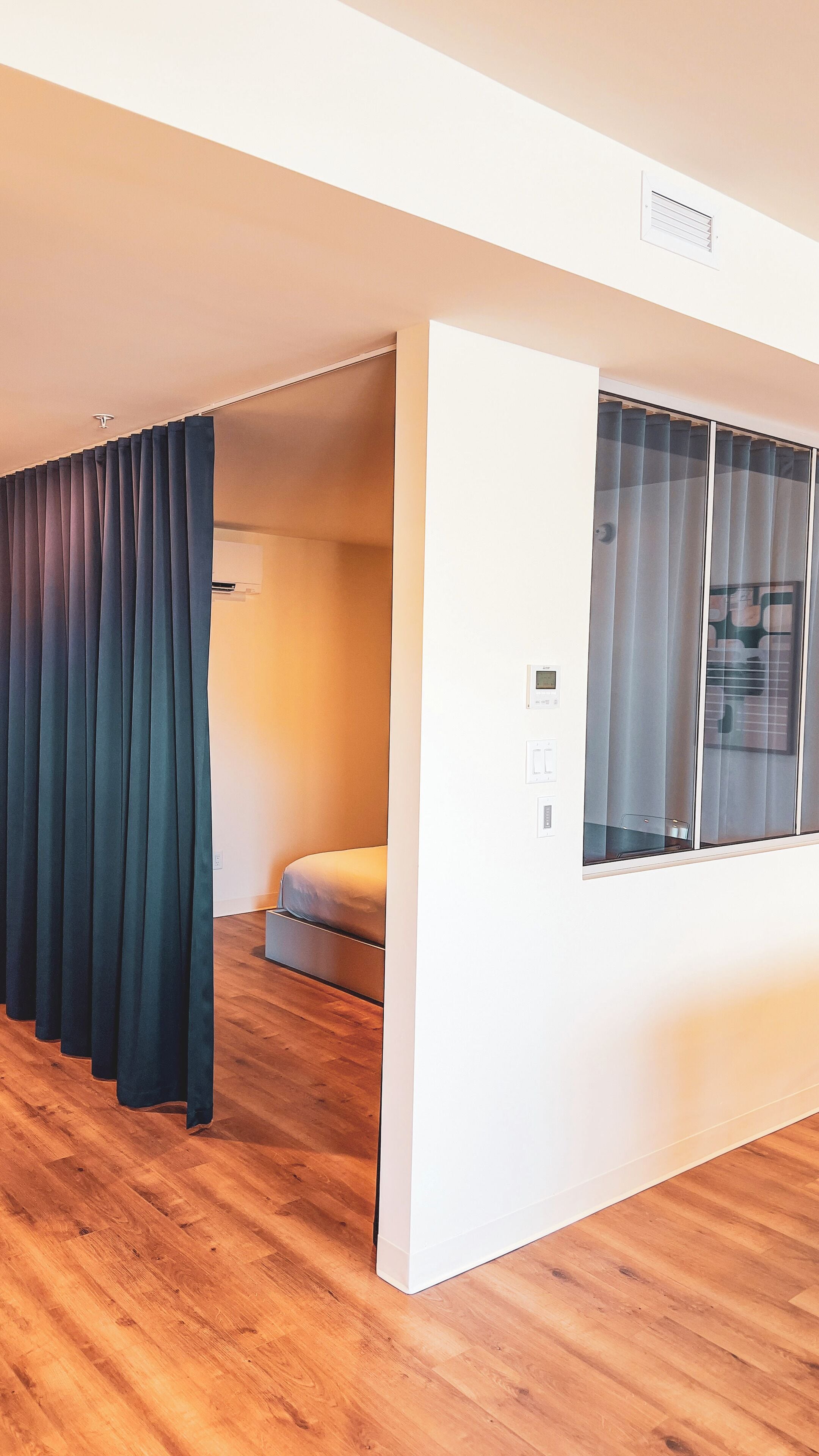 A modern room with a large window, a bed, and a built-in air conditioning unit.