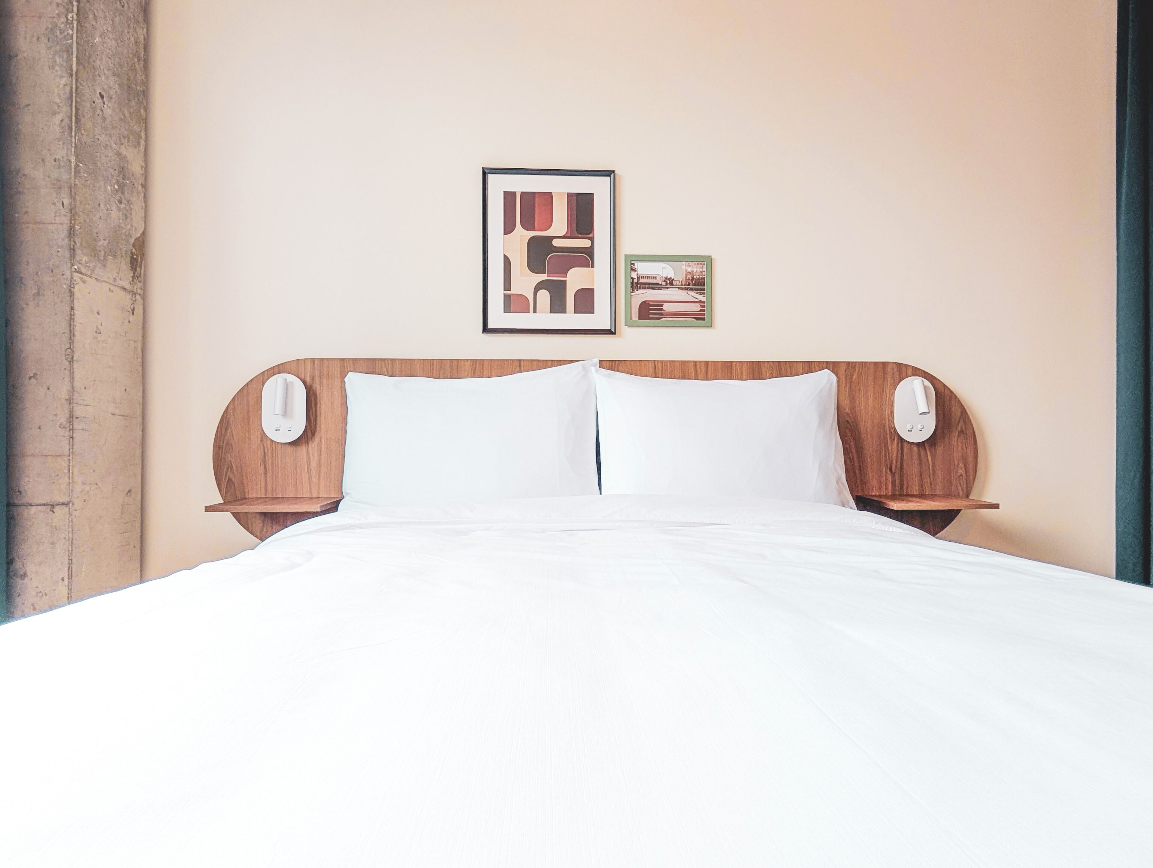 Una cama impecable con sábanas blancas, cabecera de madera y dos mesitas de noche con lámparas.