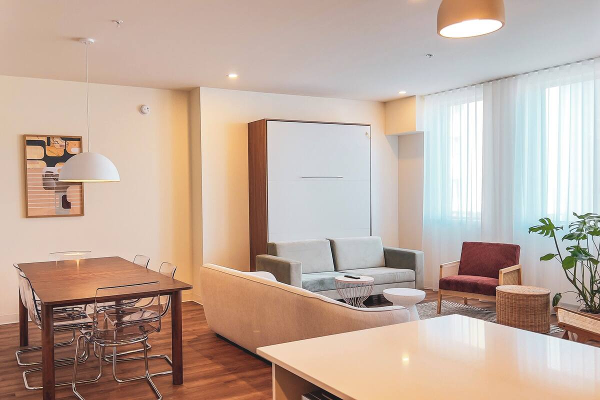 Uma sala de estar moderna com uma mesa de jantar de madeira, um sofá e uma poltrona vermelha.