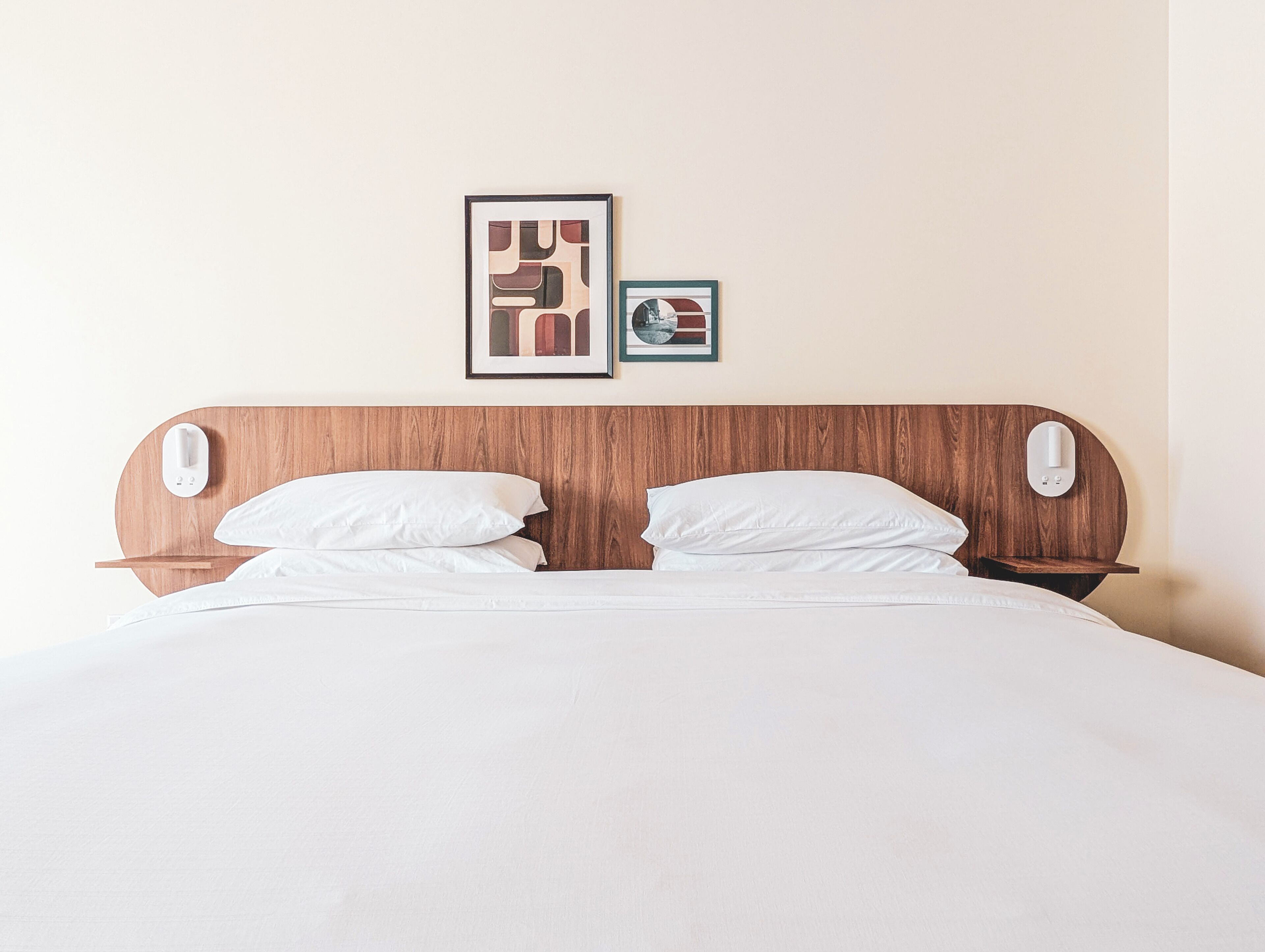 Una cama bien hecha con cabecera de madera, dos almohadas blancas y una mesita de noche con lámpara.