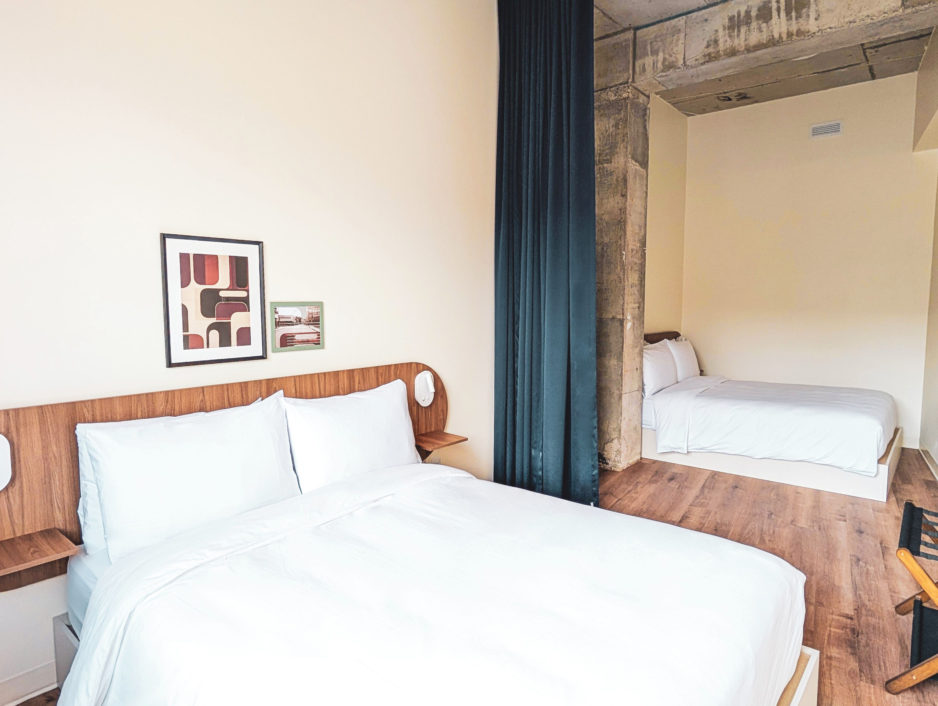 A hotel room with a large bed, a smaller bed, a wooden headboard, a nightstand, and a wall-mounted picture.
