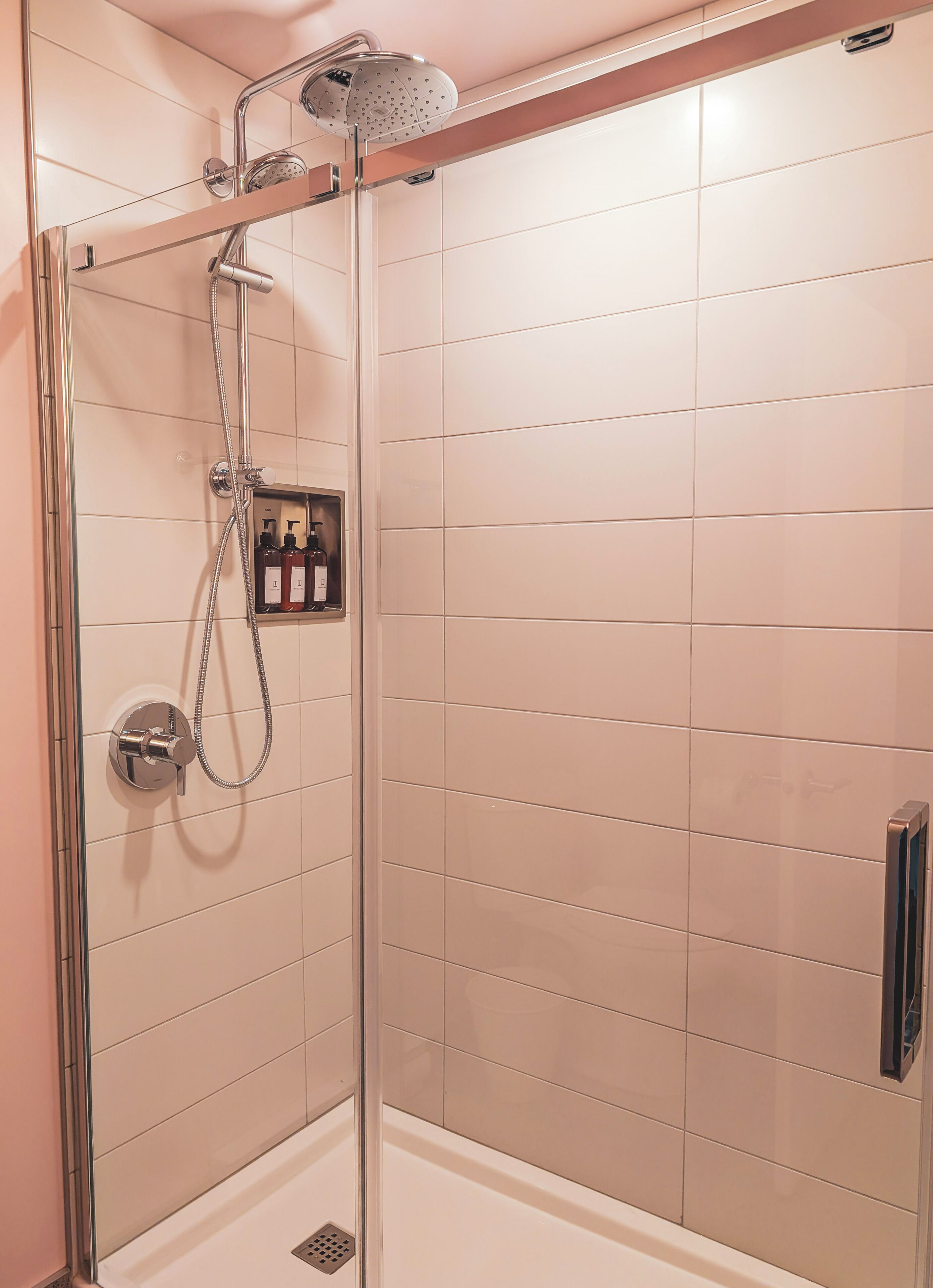 Une douche à l’italienne avec une porte en verre, une pomme de douche à main et un flexible de douche.