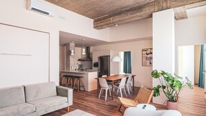 A modern living room with a sofa, a dining area with chairs, a kitchen with a stove and refrigerator, and a large window with curtains. - Terminus Hôtel (Québec)
