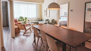 A modern living room with a wooden dining table, cushioned seating, and a large window with sheer curtains. - Terminus Hôtel (Québec)