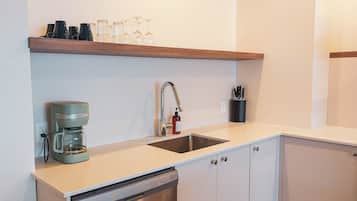 A modern kitchen with a built-in dishwasher, a coffee maker, a stainless steel sink, and a shelf with glassware.