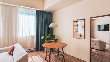 A modern living room with a sofa, a round table, a potted plant, a wall-mounted TV, and a framed picture.