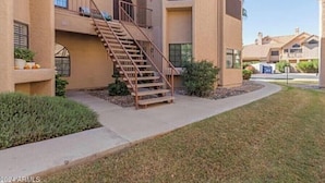 A multi-story residential building with a central staircase, balconies, and a well-maintained lawn. - Cozy and convenient Condo (Mesa)