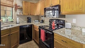 A kitchen with wooden cabinets, a black stove, a microwave, and a dishwasher. - Cozy and convenient Condo (Mesa)