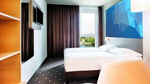 Habitación de hotel con cama, televisor, ventana grande y decoración geométrica en la pared.