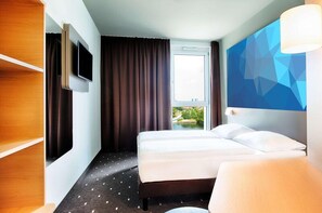 Habitación de hotel con cama, televisor, ventana grande y decoración geométrica en la pared.