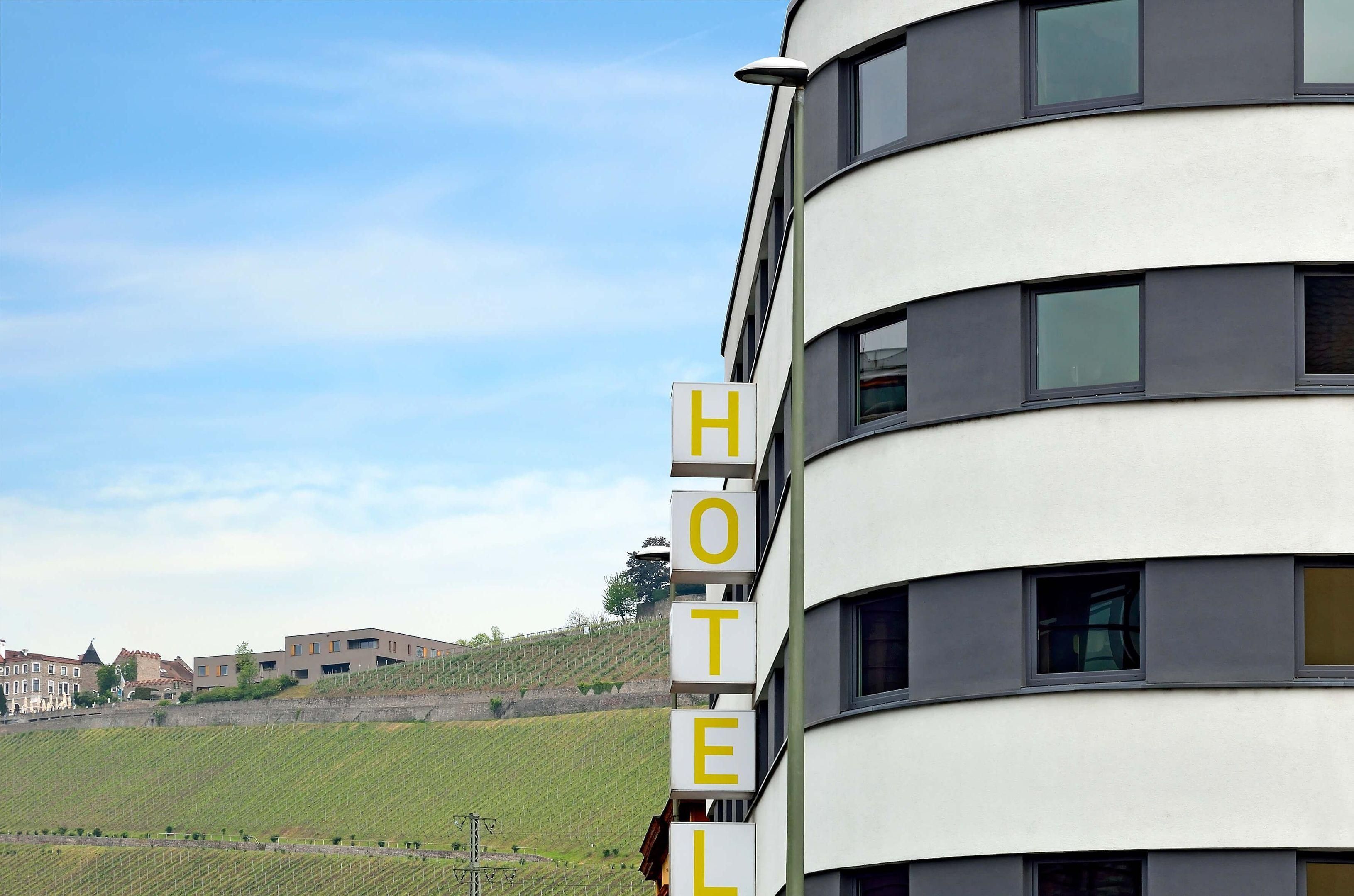 Señal de hotel en un edificio moderno con vistas a viñedos al fondo.