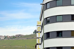 Señal de hotel en un edificio moderno con vistas a viñedos al fondo.