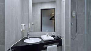 Une salle de bain moderne avec un grand miroir, un lavabo, une serviette et un espace douche.