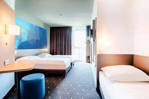 Habitación de hotel con dos camas, un escritorio, un reposapiés azul y un diseño geométrico en la pared.