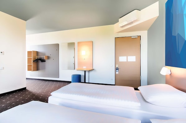 Habitación de hotel con dos camas, un armario, un espejo, un calentador de pared y una puerta.
