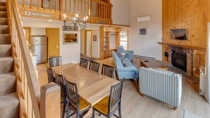 A spacious living area with a wooden staircase, a dining table with chairs, a sofa, and a fireplace. - Large Loon Condo w/Amenities (Lincoln)