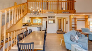 A spacious living area with a wooden staircase, a dining table with chairs, a blue sofa, and a kitchen in the background. - Large Loon Condo w/Amenities (Lincoln)