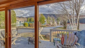 A wooden deck with a view of a road and houses, a covered area with chairs, and a surfboard rack. - Large Loon Condo w/Amenities (Lincoln)