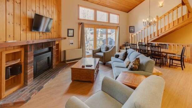 A spacious living room with a fireplace, a television mounted on the wall, and a dining area with wooden furniture. - Large Loon Condo w/Amenities (Lincoln)