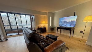 A modern living room with a leather sofa, a flat-screen TV, a lamp, and a view through large glass doors.