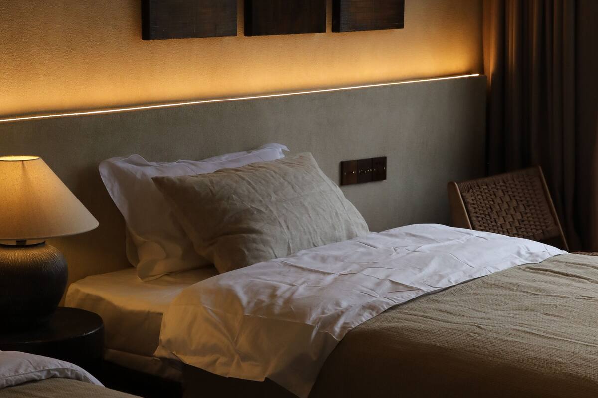 Una habitación de hotel con dos camas, una mesita de noche con lámpara y un aplique de pared.