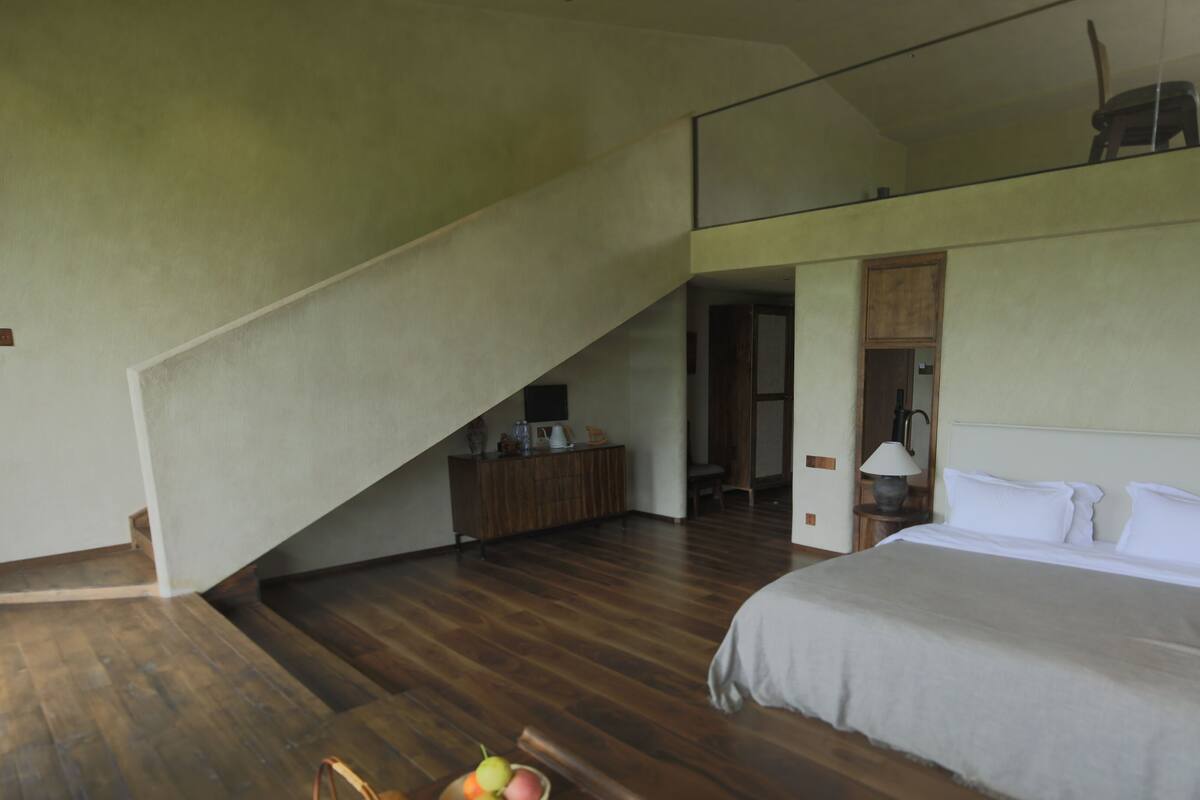 Un dormitorio con una cama grande, un escritorio de madera, una silla, una lámpara y una escalera que lleva a un nivel superior.