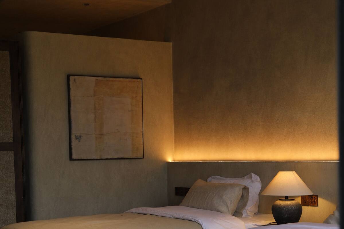 Habitación de hotel con dos camas, suelo de madera, un cuadro colgado en la pared y una lámpara de noche.