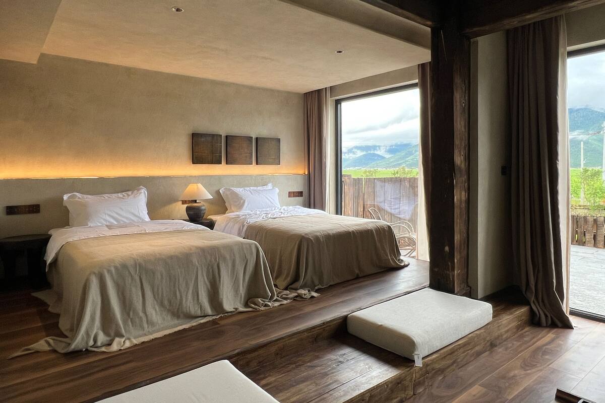Habitación de hotel con dos camas, piso de madera, ventana grande con vistas al exterior y balcón.