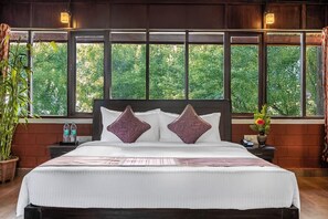 A neatly made bed with a white and pink striped bedspread, two decorative pillows, and a nightstand with a phone and a vase of flowers. - Sterling Brookstone Coorg (Madikeri)