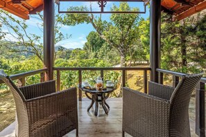 A covered outdoor seating area with wicker chairs and a table, overlooking a lush garden and distant hills.
