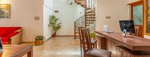 A modern hotel lobby with a wooden reception desk, a red armchair, a staircase, and potted plants.