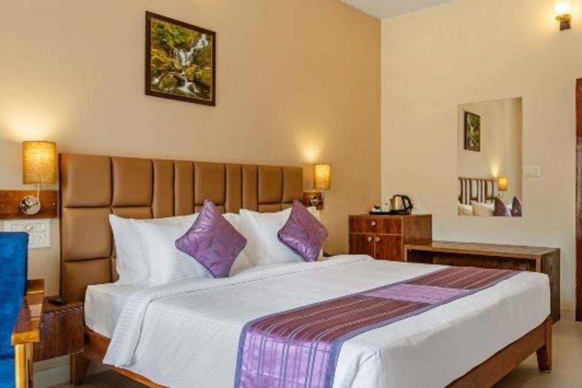 A hotel room with a bed, a nightstand, a blue chair, a wardrobe, and a mirror.