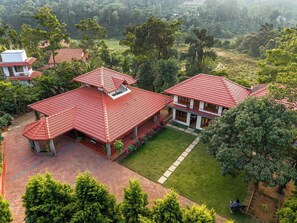 A large, two-story house with a red-tiled roof, surrounded by lush greenery and a well-maintained lawn.