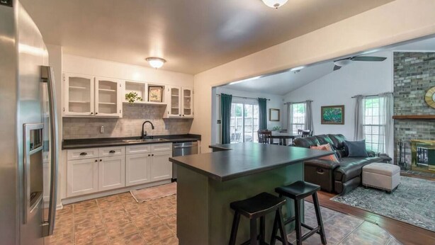 A modern kitchen with white cabinets, a central island with stools, and a dining area with a fireplace. - 10 Min. Drive From Tournament! WiFi, Parking for 3! Fire Pit! TV's In All Rooms! (Martinez)