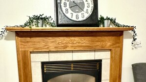 Una chimenea con un reloj encima, un repisa decorada con plantas y fuego encendido en su interior.