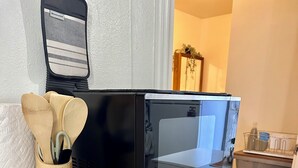 Una cocina con un microondas sobre un mueble blanco, una bandeja de madera con utensilios de cocina y un salero.