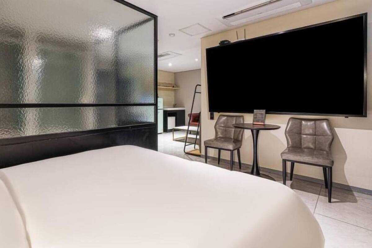 A hotel room with a large bed, a TV, two chairs, and a small table.