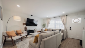 A modern living room with a sofa, armchairs, a coffee table, a flat-screen TV, and a fireplace. - Serene river view & beach walk, near Monterey Aquarium, Laguna Seca, Santa Cruz (Moss Landing)