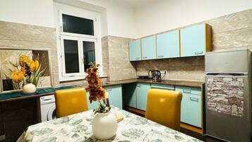 A kitchen with light blue cabinets, a white refrigerator, and a dining table with yellow chairs.