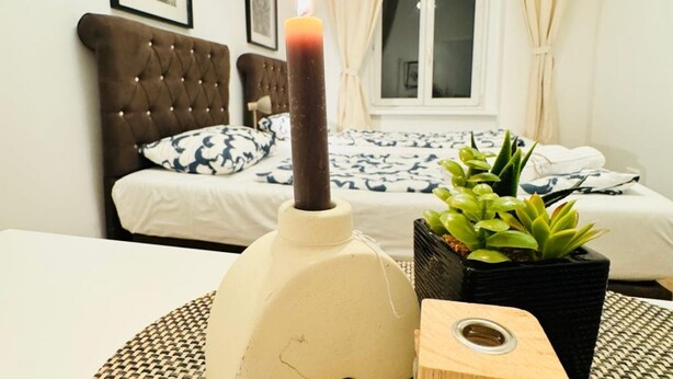 Une chambre avec un lit, une table de chevet sur laquelle se trouve une bougie et une plante en pot.