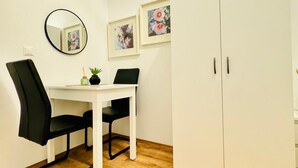 A room with a white desk, two black chairs, a round mirror, and two framed floral pictures on the wall.