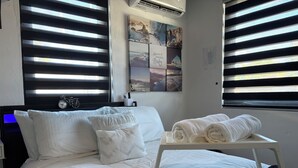 Habitación de hotel con cama, almohadas, una mesita con toallas y una pared decorada con cuadros.