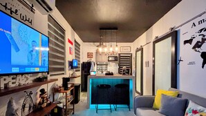 Un espacio habitable compacto con kitchenette, comedor y zona de estar con sofá y sillones.