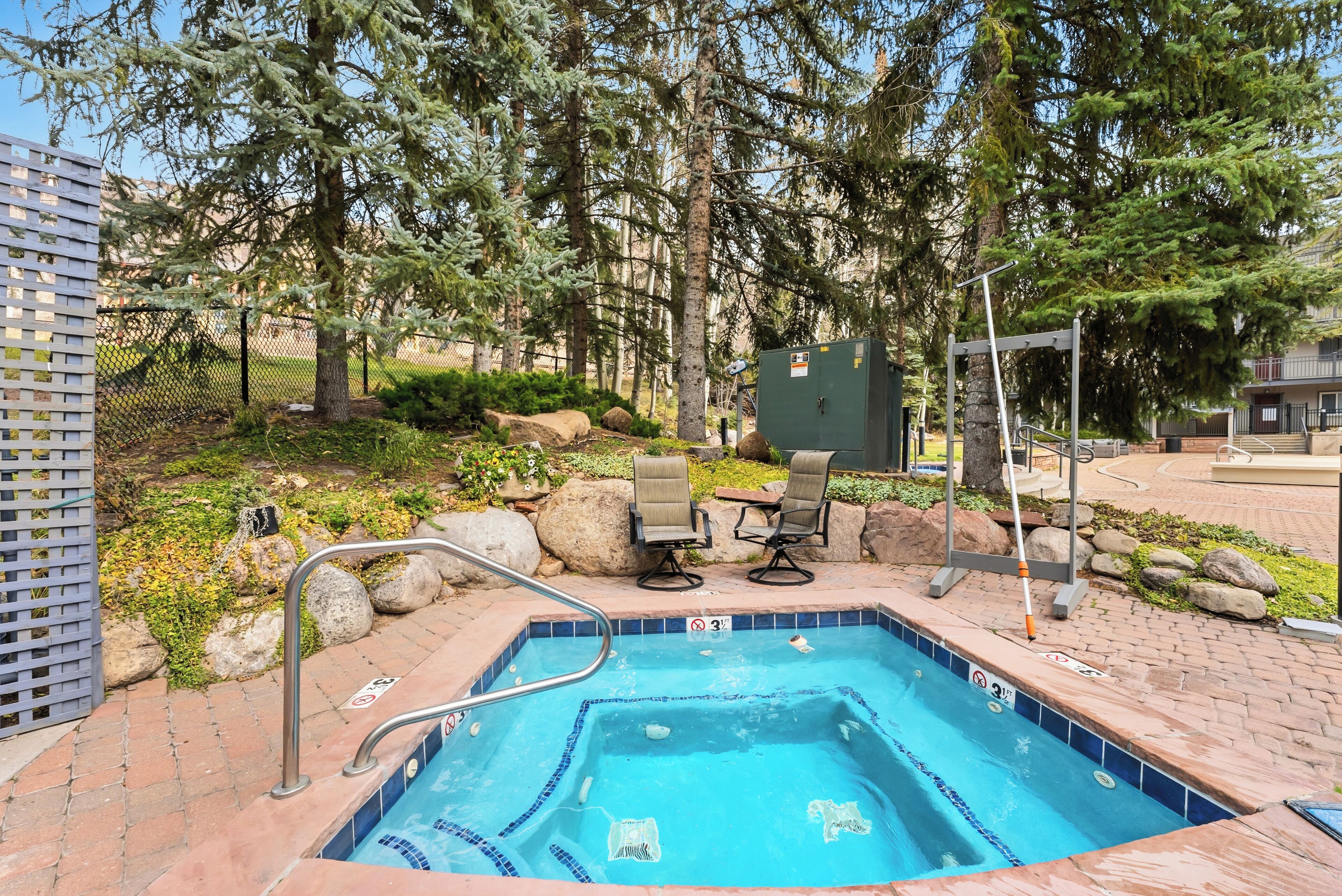 Une piscine rectangulaire aux carreaux bleus, entourée d’une terrasse en briques, avec deux chaises et une table à proximité.